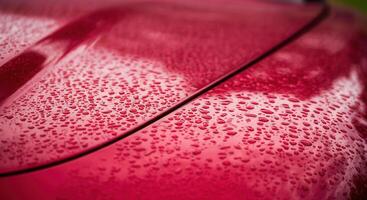 Close-up of water droplets on a dark red cherry car surface in rainy weather photo