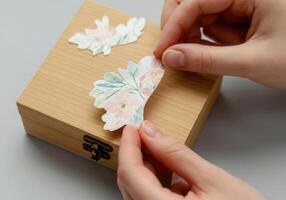 Hands applying floral paper cutout on wooden box for decoupage craft project photo