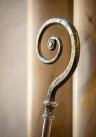 Ornate Tip of a crozier bishop staff against marble pillar in soft light photo