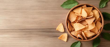 A bowl of crispy barbecue chips sits on a rustic wooden table, surrounded by fresh leaves and a few scattered chips, inviting snacking moments photo