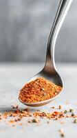 Spicy seasoning rests on a stainless spoon with scattered spices on a light stone surface, highlighting culinary creativity and flavor enhancement photo