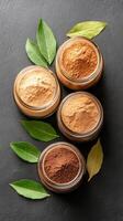 Four jars filled with various natural spices are arranged aesthetically on a dark stone surface, complemented by fresh bay leaves, perfect for culinary creativity photo