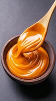 Rich and smooth caramel sauce is swirled in a wooden bowl, perfect for drizzling over ice cream, pastries, or as a dip for fruits photo
