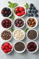 Overhead view of various nuts seeds and berries arranged in white bowls on a gray surface with mint leaves photo