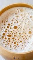 Close up of frothy light brown liquid with many bubbles in a round bamboo bowl. Foam detail and light color on light background photo