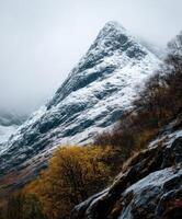 Mountain peak with snow and autumn trees in cloudy weather photo