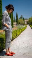Woman in stylish outfit walks through garden path in sunlight photo