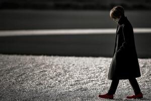 Person walking on a gray surface wearing red shoes and black coat photo