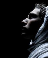 Stoic figure draped in white fabric against a dark background in a contemplative pose photo