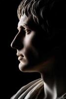 Profile of a stoic marble sculpture illuminated against a dark background photo
