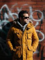 Stylish man in yellow jacket poses confidently against urban graffiti wall photo