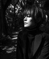 A woman in a black jacket and turtle neck sitting in the woods photo