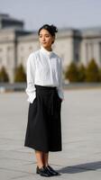 Young woman in a white blouse and black skirt poses confidently outdoors in bright sunlight photo