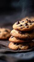 Freshly baked chocolate chip cookies stacked on a dark cloth with steam rising photo