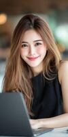 Portrait of a young woman smiling while working on a laptop in a cafe setting photo