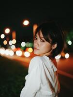 A woman in a white shirt standing in front of a street at night photo