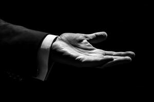 Elegant hand gesture in a formal suit, symbolizing invitation or offering against a dark backdrop photo