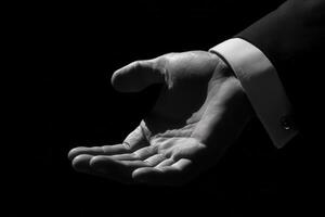Elegant hand gesture in formal attire against a dark background, inviting and poised photo