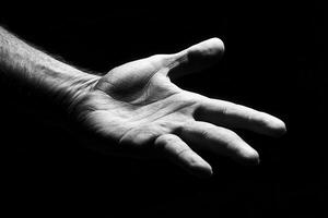 A close-up of a human hand reaching out against a black background, symbolizing connection photo