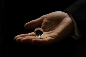 A hand holding a crystal orb reflecting light, set against a dark background photo