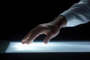 A human hand gently touches a glowing surface, creating an ethereal light effect in darkness photo
