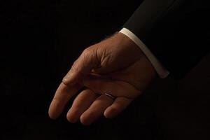Elegant hand in formal attire reaching out against a dark background, conveying invitation photo
