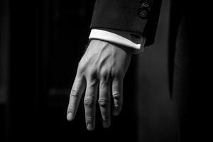 Elegant black and white close-up of a man's hand in formal attire, poised in a sophisticated setting photo