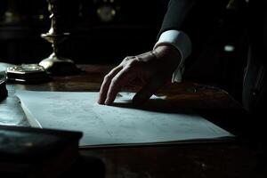 A man in a suit examines handwritten notes on a desk, surrounded by antique objects photo