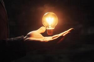 A hand holding a glowing light bulb, symbolizing innovation and creativity in a dark setting photo