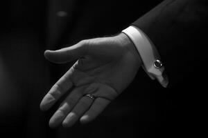 Elegant black and white image of a hand reaching out, showcasing a wedding ring and cufflink photo