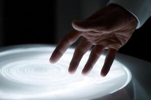 A human hand gently interacts with a glowing circular light display, creating mesmerizing patterns photo