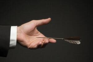 Elegant hand holding a feathered arrow against a dark background, symbolizing precision and focus photo