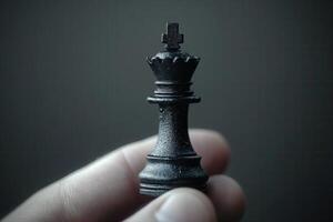 A close-up of a hand holding a black chess king piece against a dark background photo