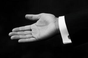 Elegant black and white image of a man's outstretched hand in a formal suit against a dark backdrop photo