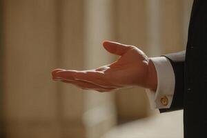 Elegant hand gesture of a suited individual against a blurred architectural backdrop photo