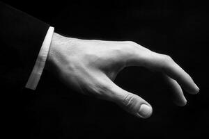 Elegant black and white image of a reaching hand in a formal suit against a dark backdrop photo