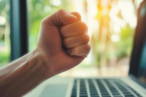 Determined hand clenched in a fist above a laptop, symbolizing focus and resolve in a bright workspace photo