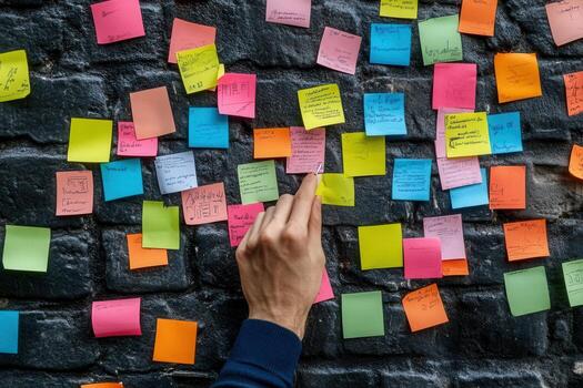 A hand selecting a sticky note from a colorful wall of notes in an urban workspace setting photo
