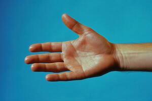 A human hand reaching out against a blue background, showcasing skin texture and details photo