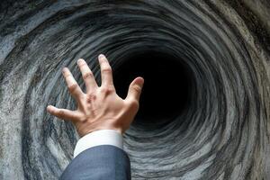 A businessperson reaches into a dark tunnel, symbolizing uncertainty and challenges ahead photo