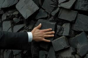 A businessman in a suit touching a textured stone wall, symbolizing strength and resilience photo