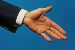 A business professional extends a hand for a handshake against a blue background photo
