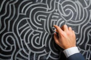 A hand navigating a complex chalk maze on a blackboard, symbolizing problem-solving photo
