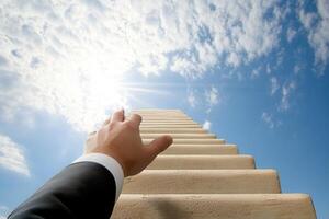 A business professional reaching for success while climbing a stairway to the clouds photo