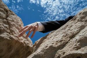 A businessman in a suit reaches out from between two rocky cliffs under a blue sky photo