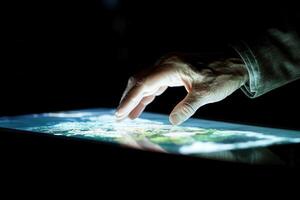 Hand interacting with a touchscreen displaying a detailed map of the Earth at night photo