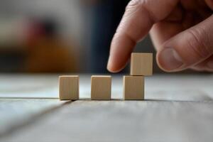 Hand placing a wooden block on top of smaller blocks on a table, showcasing creativity and focus photo