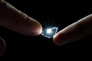 Two fingers reaching towards a sparkling diamond, illuminated against a dark background photo