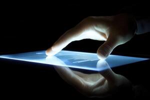 Hand interacting with a glowing tablet screen, showcasing data analysis in a dark room photo