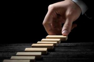 Hand poised to place wooden block in a domino arrangement on a dark wooden surface photo